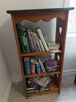 Full view of narrow wood bookshelf with green top and books for scale