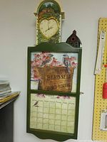Cabinet hung on wall with clock mounted atop and birdhouse beside
