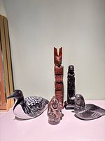 Group shot of five art pieces: wooden loon, hardwood totem, resin Inuit figure, black resin totem behind, soapstone duck