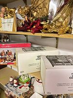 Shelving with three boxed Christmas village buildings, additional decor around
