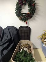 Wreath hanging on wall above open Rubbermaid tote filled with decorations