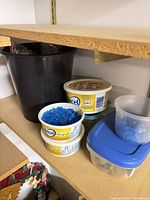 Shelf with black plastic pot, several plastic tubs containing blue stones