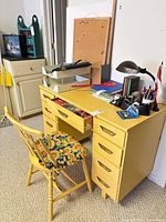 Front view of yellow desk with chair showing drawers and accessories on top