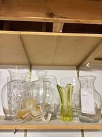 Shelf view showing seven clear vases, pale green vase and glass flower