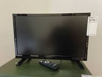Front view of Insignia 19" LED TV on stand with remote placed in front