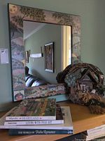 Wall mirror with painted frame, wreath and stack of books displayed