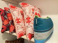 Shelf with four visible pillows: maroon floral, two white/red floral, blue striped; portion of brown pillow below
