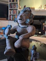 Seated terra cotta deity statue holding staff, smaller condor idol visible