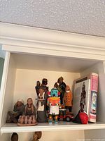 Shelf view showing assorted folk-art figurines, books, and mask