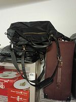 Black overnight bag atop burgundy suitcase on shelf