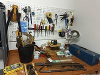 Overall view of pegboard, workbench, clamps in bucket, toolbox, lamp