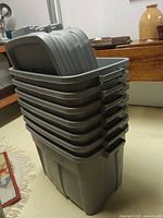 Stack of seven grey Rubbermaid Roughneck totes with lids visible