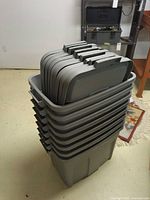 Stack of eight grey Rubbermaid totes with nine lids nested on top