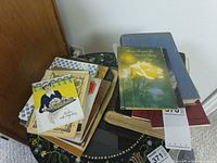 Two uneven stacks of vintage cookbooks and hardcovers on small round table