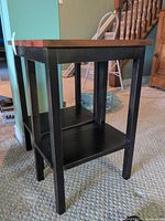full view of one side table showing pine top and dark base with lower shelf