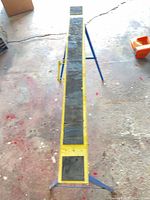Top view of folding saw horse work platform showing yellow surface, blue legs, wear and rust