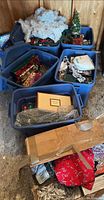 Multiple blue totes and cardboard box containing assorted Christmas decorations