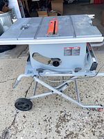 Full view of table saw on folding stand, tabletop, rip fence, wheels visible
