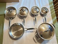 entire cookware set laid out showing 3 saucepans with lids, fry pan, larger pot with lid