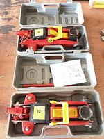 Both hydraulic floor jacks inside their moulded grey carry cases with manuals and handles visible