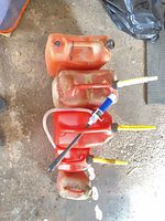 Five red plastic gas cans lined up, showing spouts and siphon pump