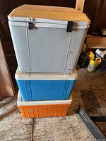 Stacked view of gray Koolatron, blue ice chest, orange Coleman cooler