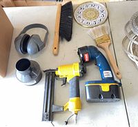 Group shot of flashlight, nailer, broom head, clock face, paint brush, earmuffs, dust fitting