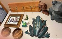 Group view of all items including large metal frog statue, wall art frog, coat rack, owl figurine, framed print, magnets, bowls