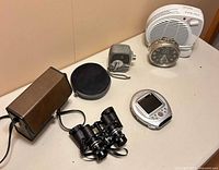 Group shot of all items: heater, clock, camera, DVD player, binoculars, two cases