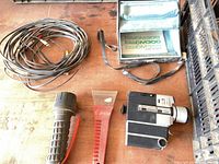 Camera, case, long cable, red scraper, tool grip and strap on tabletop