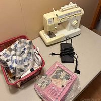 Singer sewing machine, foot pedal, Dexter Hemmer & Stitcher box, basket of thread spools on table