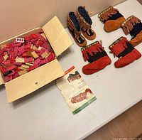Overview showing box of bricks, instruction sheet, and three pairs of moccasin booties