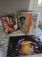All three items grouped: sealed Tupac bag, Frank Sinatra book closed, WWF magazine front cover