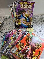 Front and side view of stacked comic books showing JSA Princes of Darkness and other titles