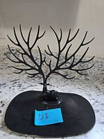 Front view of assembled black plastic tree branch jewelry stand on oval base