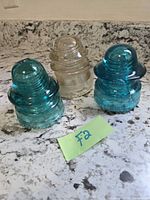 Front view of two aqua blue and one clear glass insulators on countertop