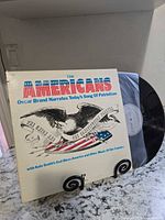 Front cover of The Americans LP sleeve and partially exposed vinyl record