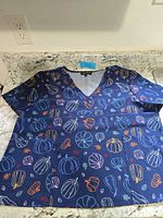 Full view of navy pumpkin-print scrub top laid flat