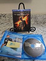 Front view showing slipcover artwork of The Dark Knight Rises and open case with discs and insert