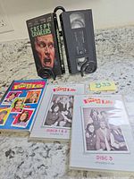 DVD set outer sleeve, two internal disc holders and VHS tape on stand