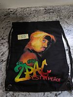 Front side of black drawstring bag with colour Tupac portrait and 2PAC Rest In Peace text