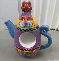 Front view of multicoloured ceramic cat teapot showing cat face, star lid, spout, handle and body cutout