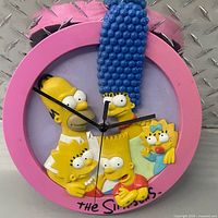 Front view showing pink frame, lavender dial, black hands, 3D Simpsons family figures