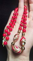 Necklace draped on hand showing red beads, gold spacers and three focal art glass beads