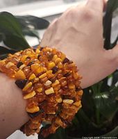 Multiple wraps of amber chip necklace around wrist showing chip size and color