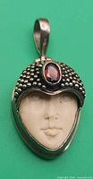 Front view of sterling silver pendant showing carved face, garnet, and bail