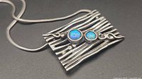 Front view of textured sterling silver pendant with two blue opal cabochons on snake chain