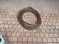 Coiled brown garden hose on brick patio