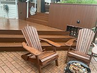 Two stained pine Adirondack chairs on brick patio beside deck