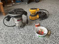 Router, sander, bits container and packet laid out on floor